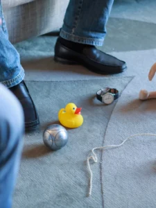 Symbole am Boden, z.B. Gummiente, Seil, Kugel. Man sieht auch noch Füsse